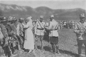 Queen Marie in a white uniform and officers decorating Romanian soldiers lined up on a field, at the front