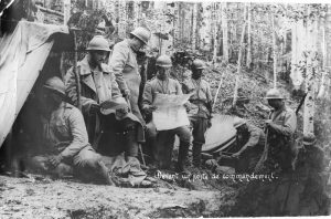 Soldiers in helmets near a military tent in the forest, consulting a map at a command post