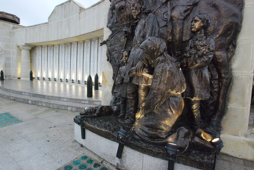 Bronze sculpture of peasants at the Mărăști Mausoleum with illuminated memorial plaques in the background