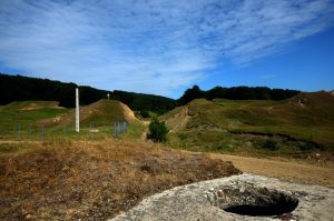 Concrete ruin of the water basin in Mărăști, near green hills and a white cross in the distance