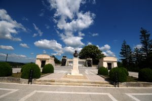 Bust of Marshal Averescu on a stone pedestal in front of the Mărăști Mausoleum under a sunny sky with clouds