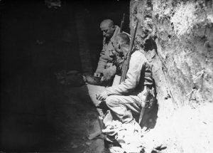Two Romanian soldiers sitting in a deep trench, holding rifles and smoking during World War I