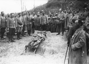 Officers, soldiers, and a priest gathered at the funeral of a French lieutenant lying on a stretcher