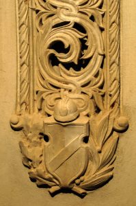Stone relief carving of a military helmet resting on a shield surrounded by decorative leaves