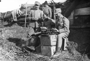 Soldiers on the front line in trenches, one typing on a typewriter placed on military crates
