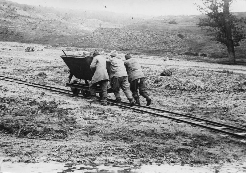 Three men pushing a tip cart along narrow-gauge railway tracks