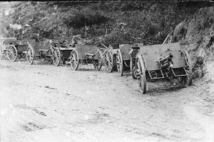 Artillery guns and howitzers lined up along the side of a dirt road