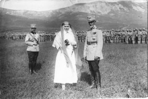 Queen Marie in a nurse uniform and King Ferdinand I standing in a field before lined troops