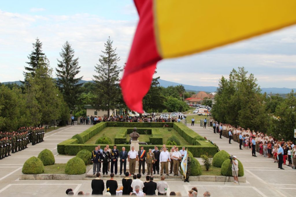 Ceremony at Mărăști seen from above, with officials, soldiers, and public gathered near a bust and flag in foreground