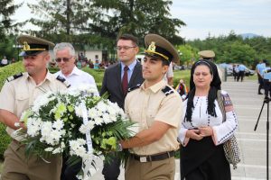 Military officers carrying a white flower wreath, followed by officials and a woman in folk costume at Mărăști