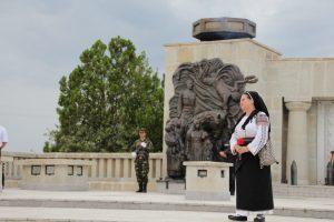 Maria Murgoci in folk costume singing at Mărăști Mausoleum, near a bas-relief and a soldier on guard