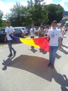 Young people carrying a large Romanian flag along a road, wearing commemorative Mărăști 1917-2017 t-shirts
